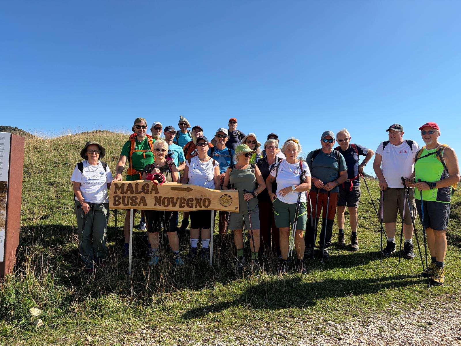 I soci del CISV posano insieme davanti al cartello in legno che indica Malga Busa Lovegno, immersi nel paesaggio montano e nella bellezza dell’escursione condivisa.